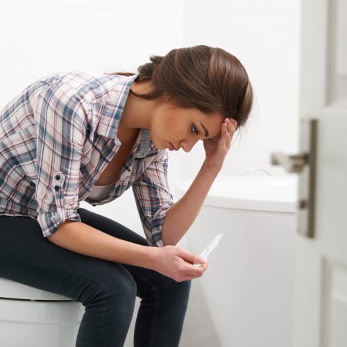 Teenage Girl Sitting In Bathroom With Pregnancy Test